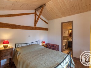 A bedroom with a bed, two bedside tables with lamps, wooden beams on the ceiling, and a bathroom visible through an open door. - Rustic cottage with 2 bedrooms, nature, pets allowed, wifi and parking (Montilliers)