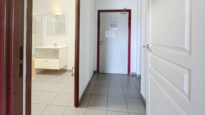 En gang med en hvid dør, en rød dørkarm, og et hvidt badeværelse med spejl og vask.