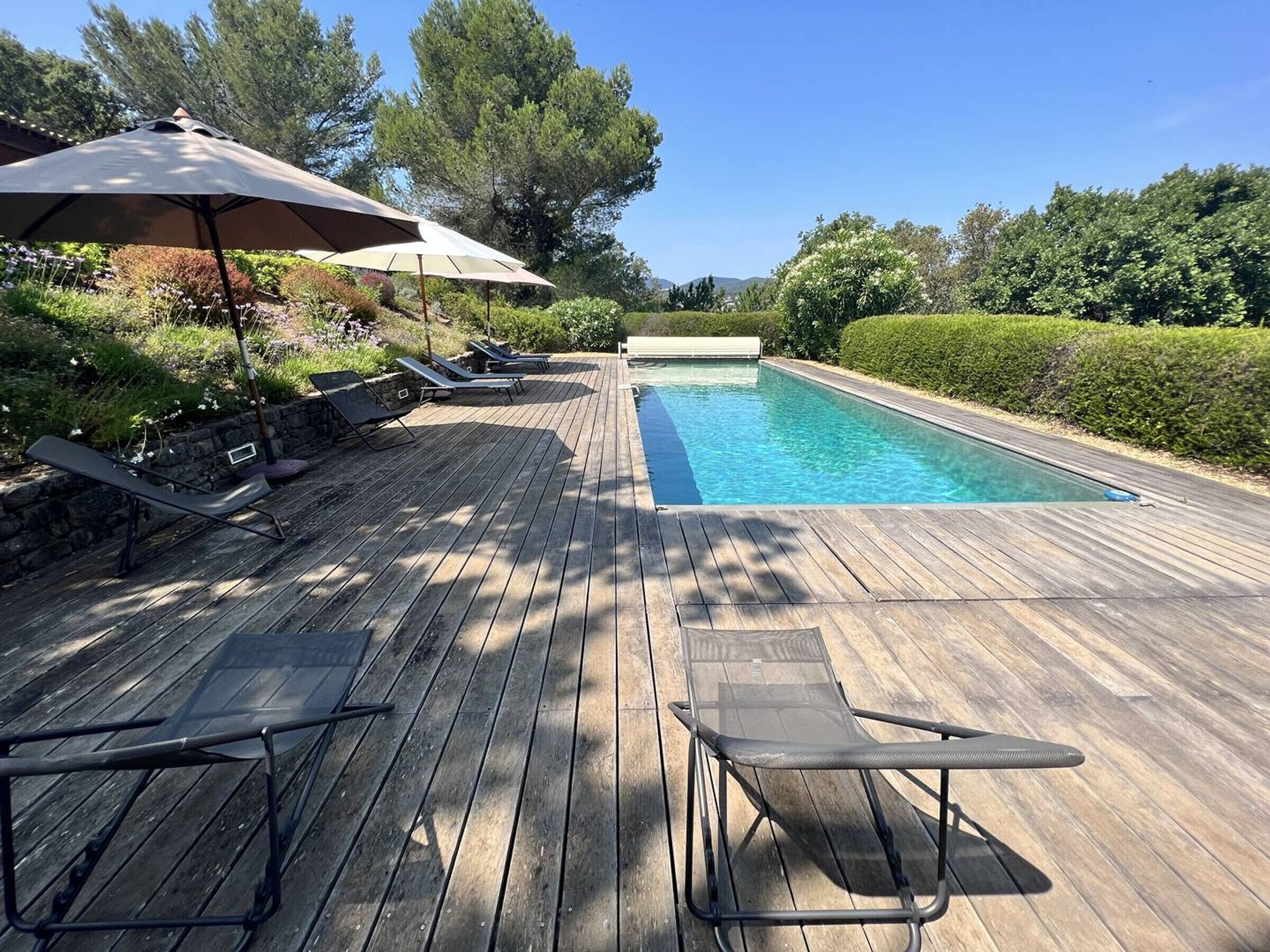 A wooden deck with a swimming pool, lounge chairs, and umbrellas.