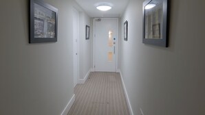 Un couloir avec un tapis à rayures, des tableaux encadrés accrochés aux murs et une porte au fond.
