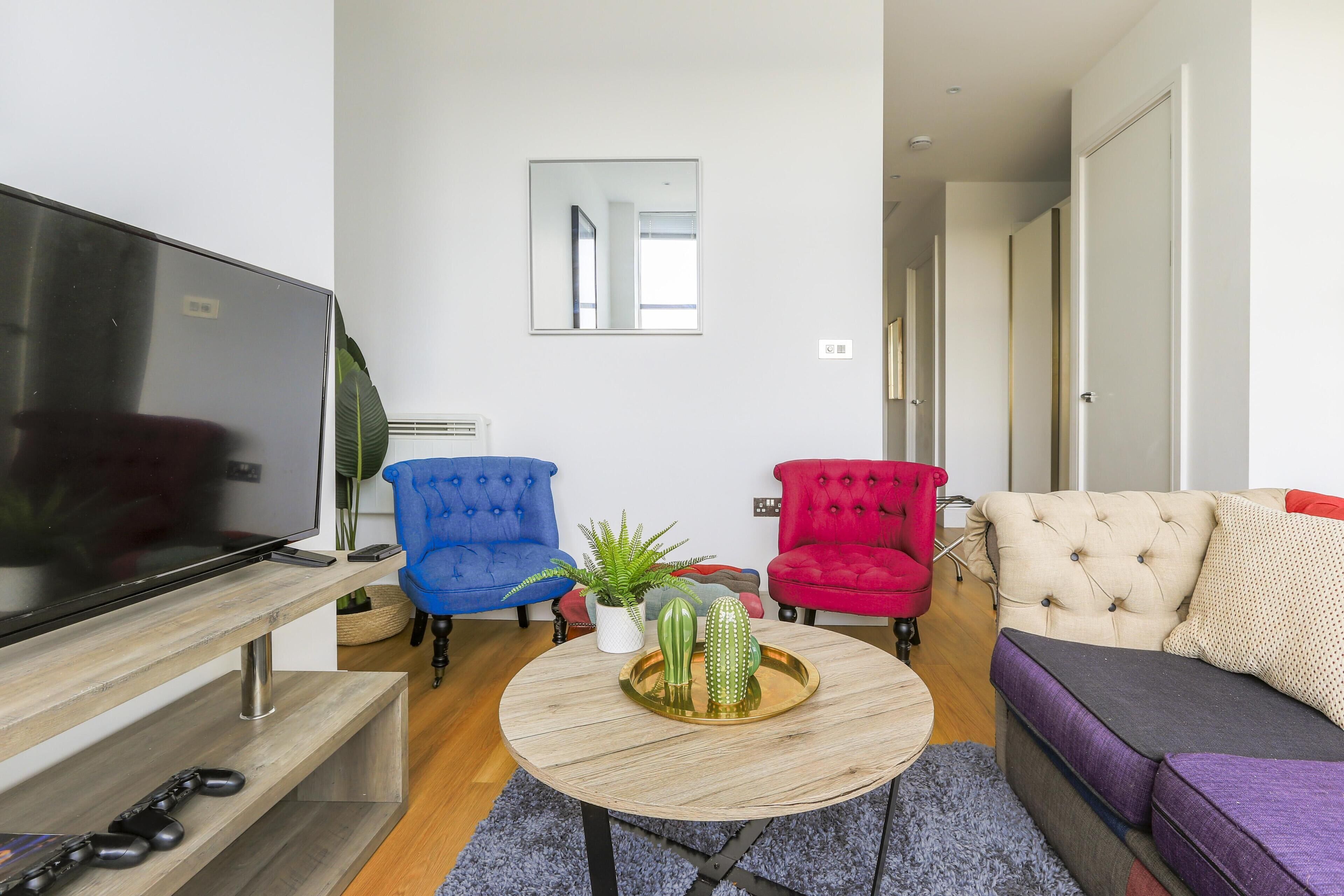 Una sala de estar moderna con un televisor de pantalla plana, una mesa de centro con objetos decorativos, un sofá y dos sillones.