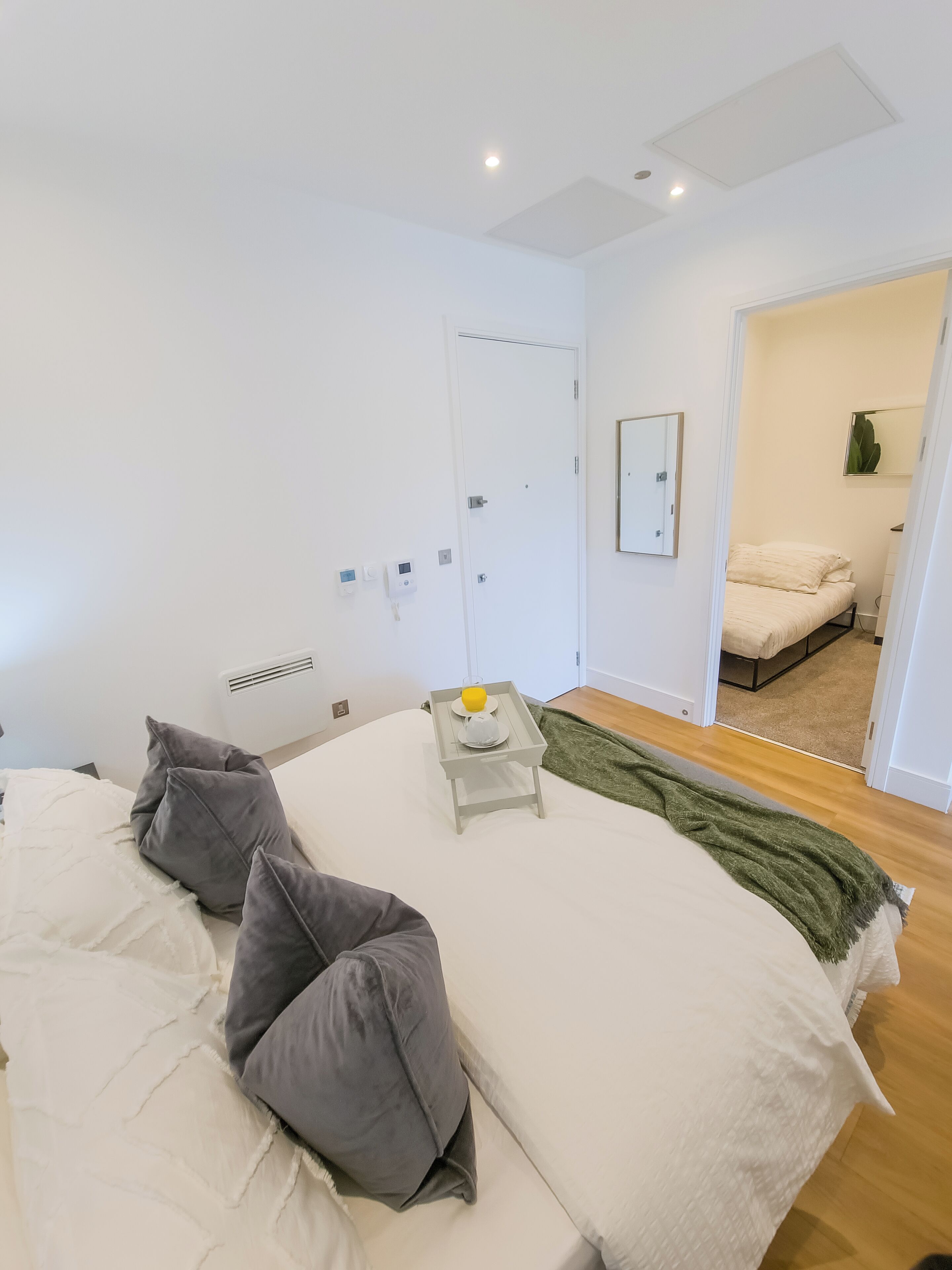 Un dormitorio con una cama, almohadas, una mesita de noche con una bandeja, una puerta y un espejo.