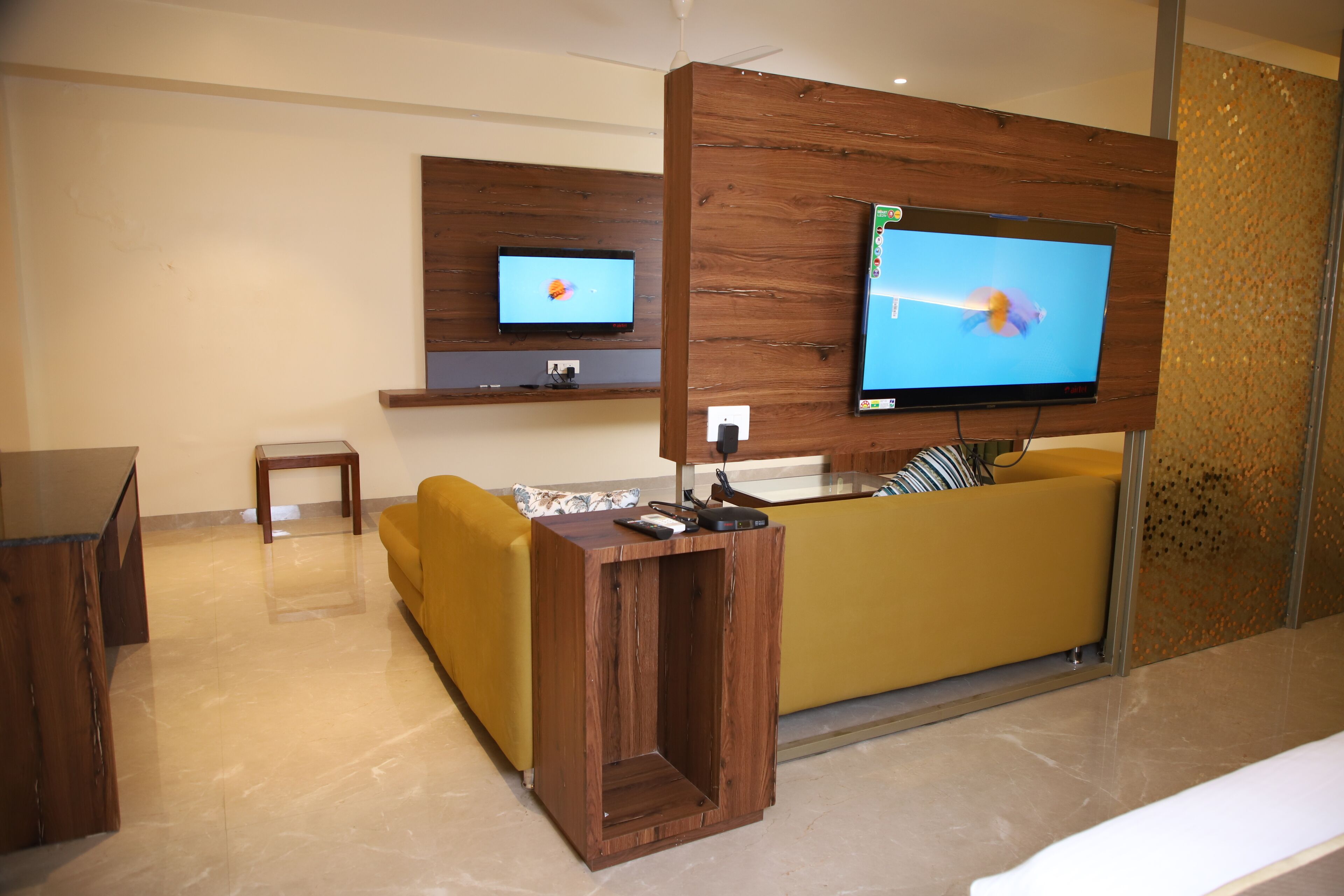 Una sala de estar moderna con un sofá amarillo, una mesa de centro de madera y un televisor de pantalla plana montado en un panel de madera.
