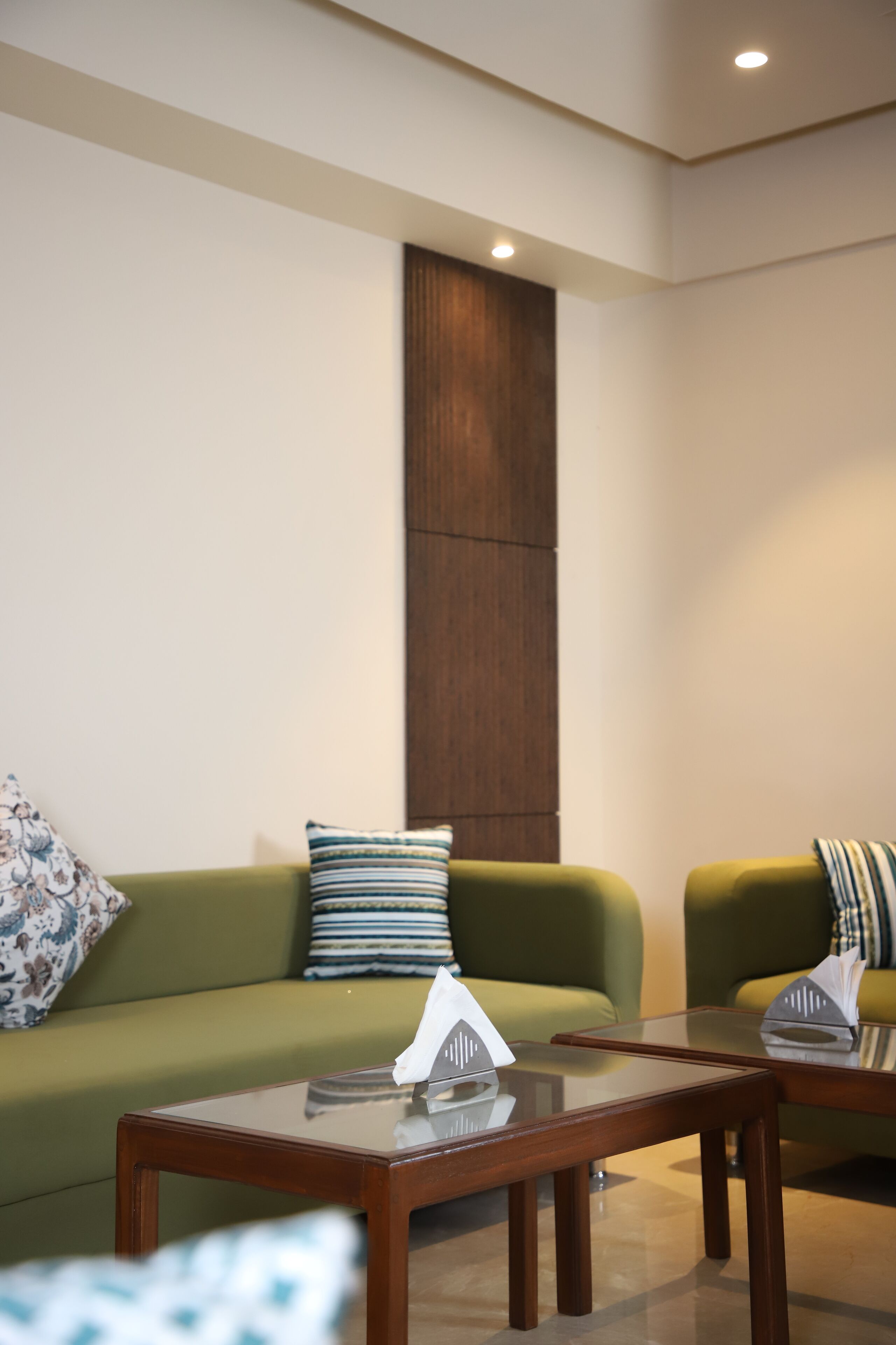 A modern living room with a green sofa, a glass coffee table, and a wooden accent wall.
