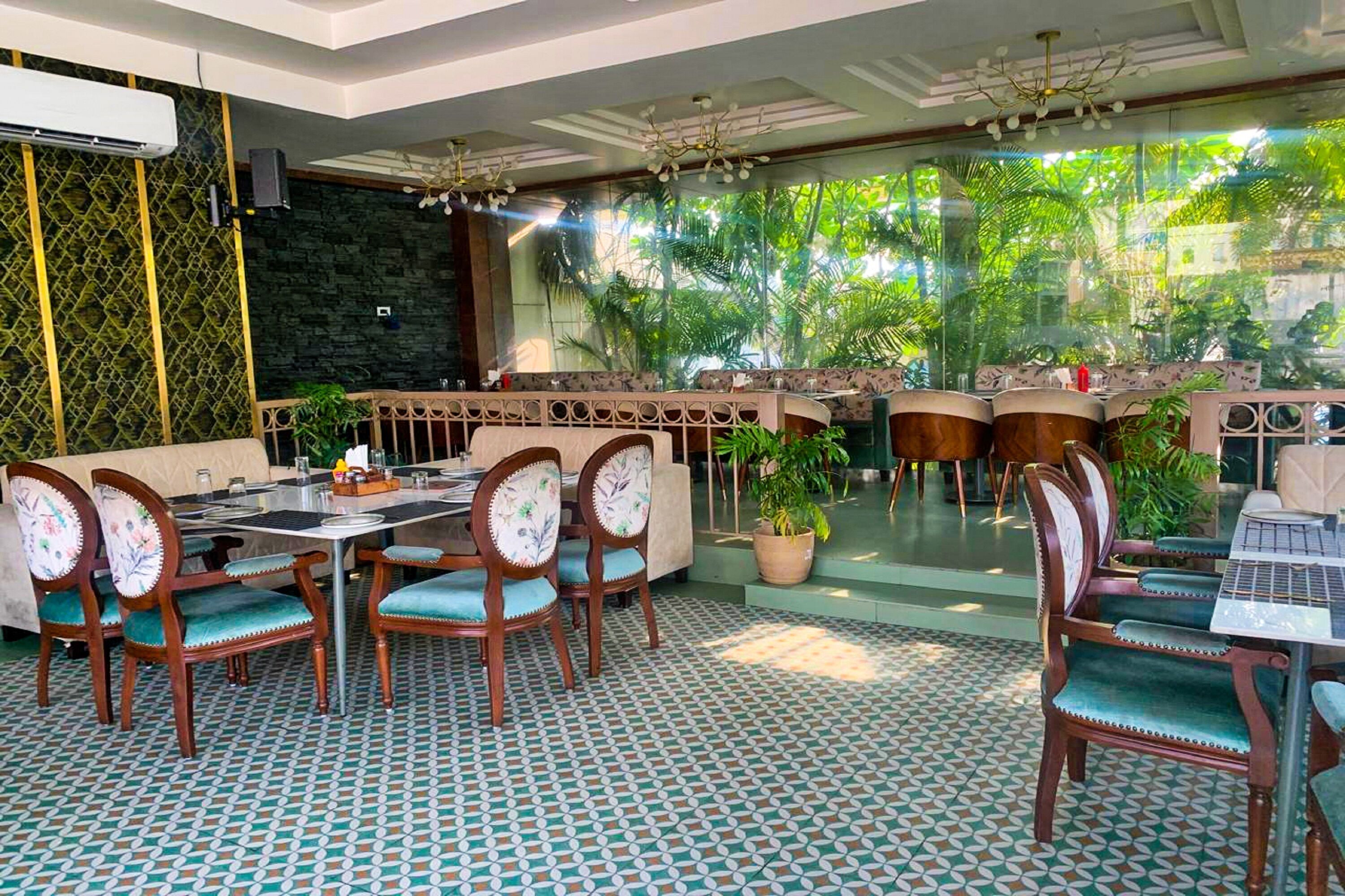 Un restaurante con piso estampado, sillas de madera con tapicería floral y vistas a zonas verdes a través de amplios ventanales.
