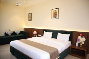 A hotel room with a large bed, a green sofa, two framed pictures on the wall, and a nightstand with a vase of flowers. - Pink Villa Boutique Hotel (Meerut)