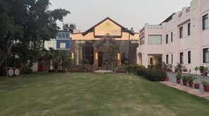 A building with a sign reading 'GLASSHOUSE' and a well-maintained lawn with potted plants. - Pink Villa Boutique Hotel (Meerut)