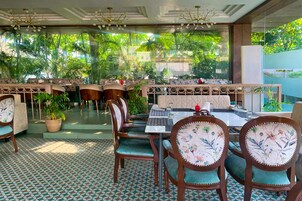An indoor dining area with wooden tables and chairs, surrounded by large windows with a view of lush greenery.