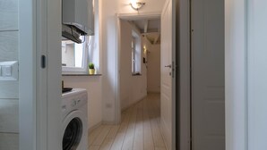 Un espace buanderie comprenant un lave-linge, une plante en pot et un couloir menant à une autre pièce.
