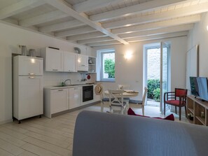 Eine moderne Küche mit weißen Schränken, ein Essbereich mit rundem Tisch und Stühlen sowie ein Fernseher auf einem Holzregal.