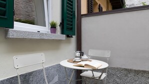 Un petit espace extérieur aménagé avec une table et deux chaises, un pot de fleurs et une fenêtre avec des volets.
