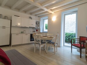 Une cuisine moderne avec des meubles blancs, un coin repas doté d’une table ronde et de chaises, et une grande fenêtre offrant une vue sur la verdure à l’extérieur.