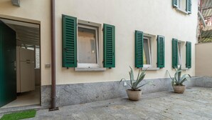 Une façade d’immeuble avec des volets verts, des plantes en pot et une entrée pavée de pierres.