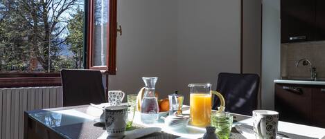 Une table de petit-déjeuner avec une carafe de jus d’orange, une cafetière et une tasse, placée sur un balcon d’où l’on peut admirer des arbres et un immeuble.