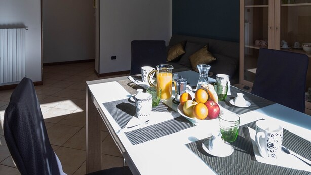Un coin repas avec une table mise pour le petit-déjeuner, comprenant des fruits, une carafe de jus d’orange, ainsi que différentes tasses et verres.