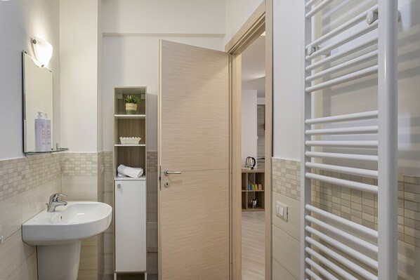 A modern bathroom with a white sink, a mirror, a towel rack, and a wooden door.