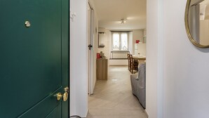 A hallway leading to a dining area with a table and chairs, a window with curtains, and a green door with a lock. - Comfy Apartment Near the Harbor by Wonderful Italy (Genoa)