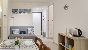 A dining area with a table set for four, a sofa, and a bookshelf with various items. - Comfy Apartment Near the Harbor by Wonderful Italy (Genoa)