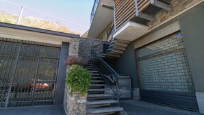 A residential building with a stone staircase leading to a wooden balcony, a garage door, and a gated entrance. - La Soliva Big House in Bellano (Bellano)