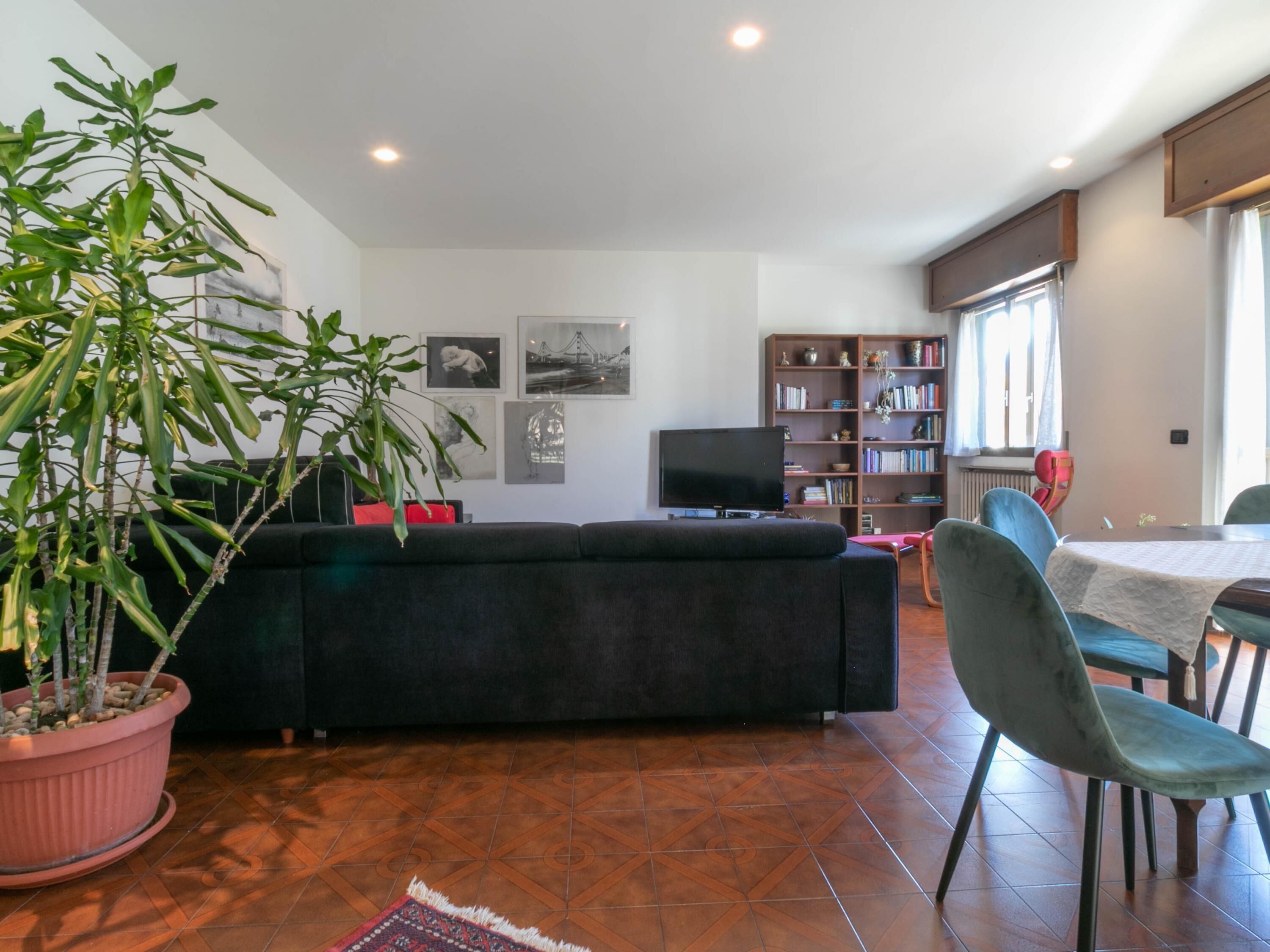 Ein Wohnzimmer mit einer Couch, einem Fernseher, einem Bücherregal und einem Essbereich mit Stühlen und einem Tisch.
