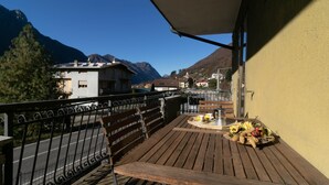 A wooden deck with a table and chairs, overlooking a mountain landscape with buildings in the background. - La Soliva Big House in Bellano (Bellano)