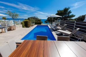 Ein Poolbereich mit Holzterrasse, Liegestühlen und Sonnenschirmen.