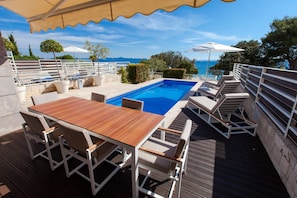 Ein Poolbereich mit Holztisch und Stühlen, einem Pool und Sonnenschirmen.