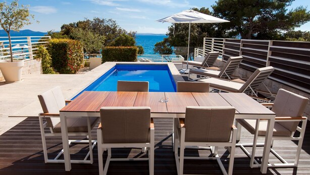 A wooden deck with a pool, lounge chairs, and a table. - Villa Calla Zadarvillas (Zadar)