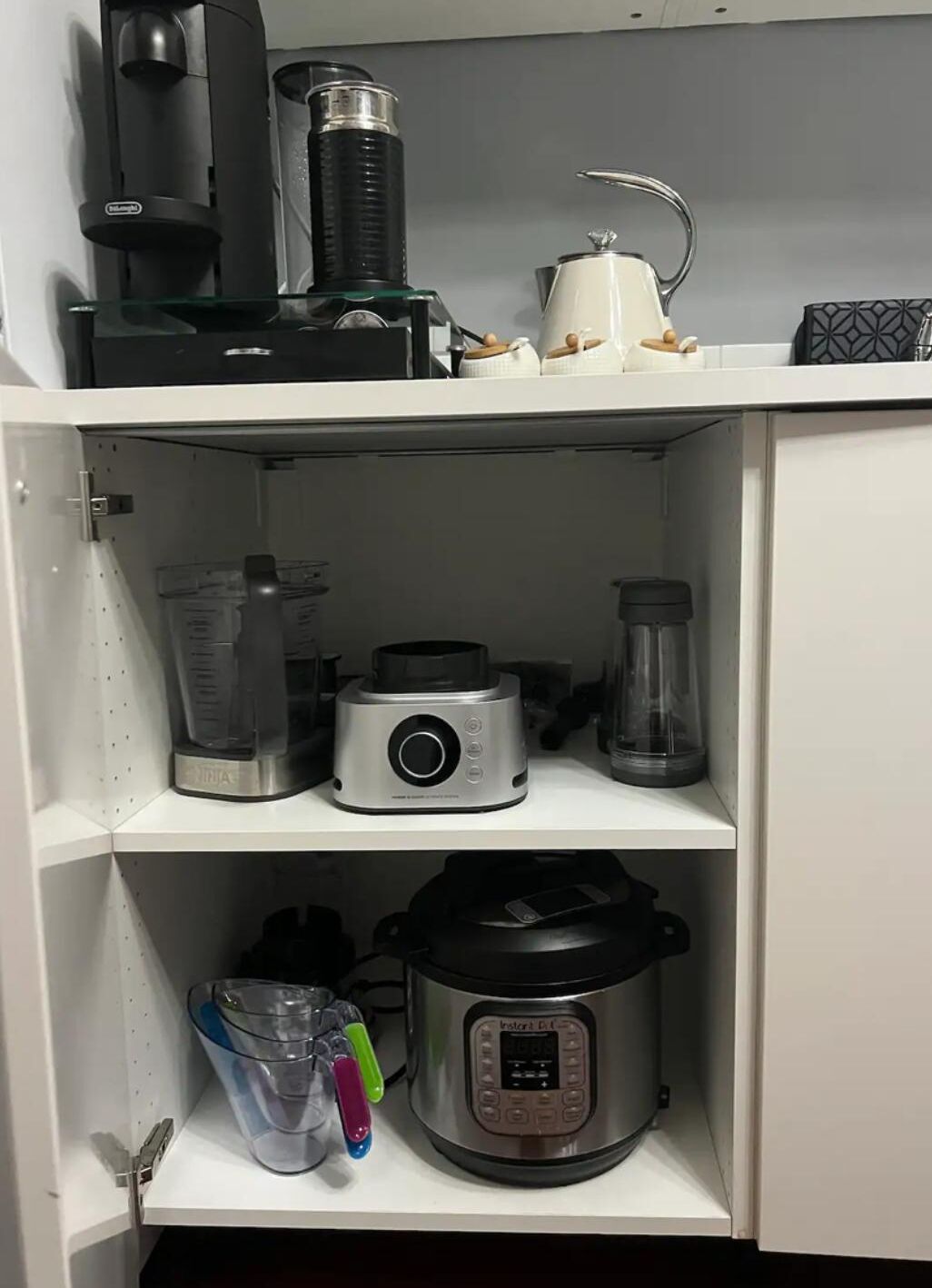 Eine Küche mit Kaffeemaschine, Mixer, Wasserkocher und Slow Cooker auf Regalen.
