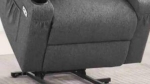 Una silla reclinable gris con reposacabezas y reposabrazos, sobre un piso alfombrado.