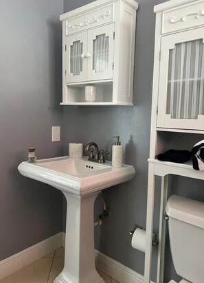 Un baño con lavamanos pedestal, dos armarios con puertas de cristal y un inodoro.