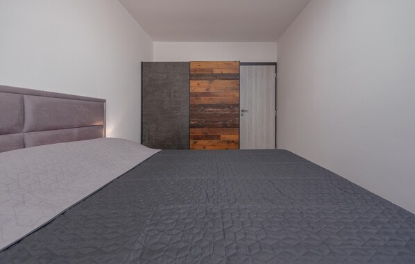 Een moderne slaapkamer met een grijs gewatteerde spreidekbed, een hoofdbord en een wand van houten panelen.