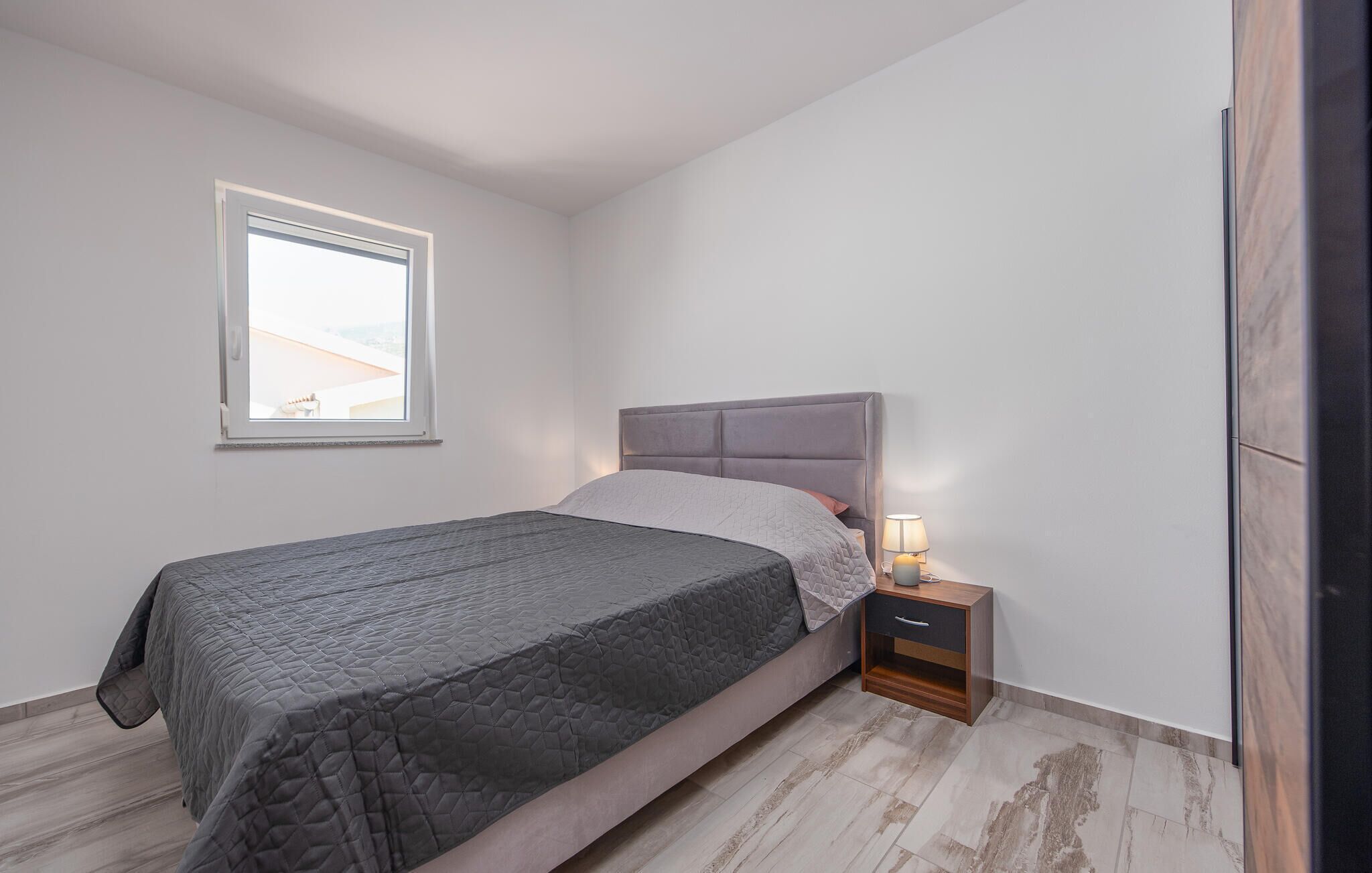 Un dormitorio con una cama, una mesita de noche, una lámpara y una ventana.
