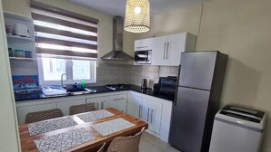 A compact kitchen with a dining table, chairs, a microwave, a stove, and a refrigerator. - Le Mirage Cozy Beach Apartment, 5 min walk to the beach. Enjoy sunset view (Flic en Flac)