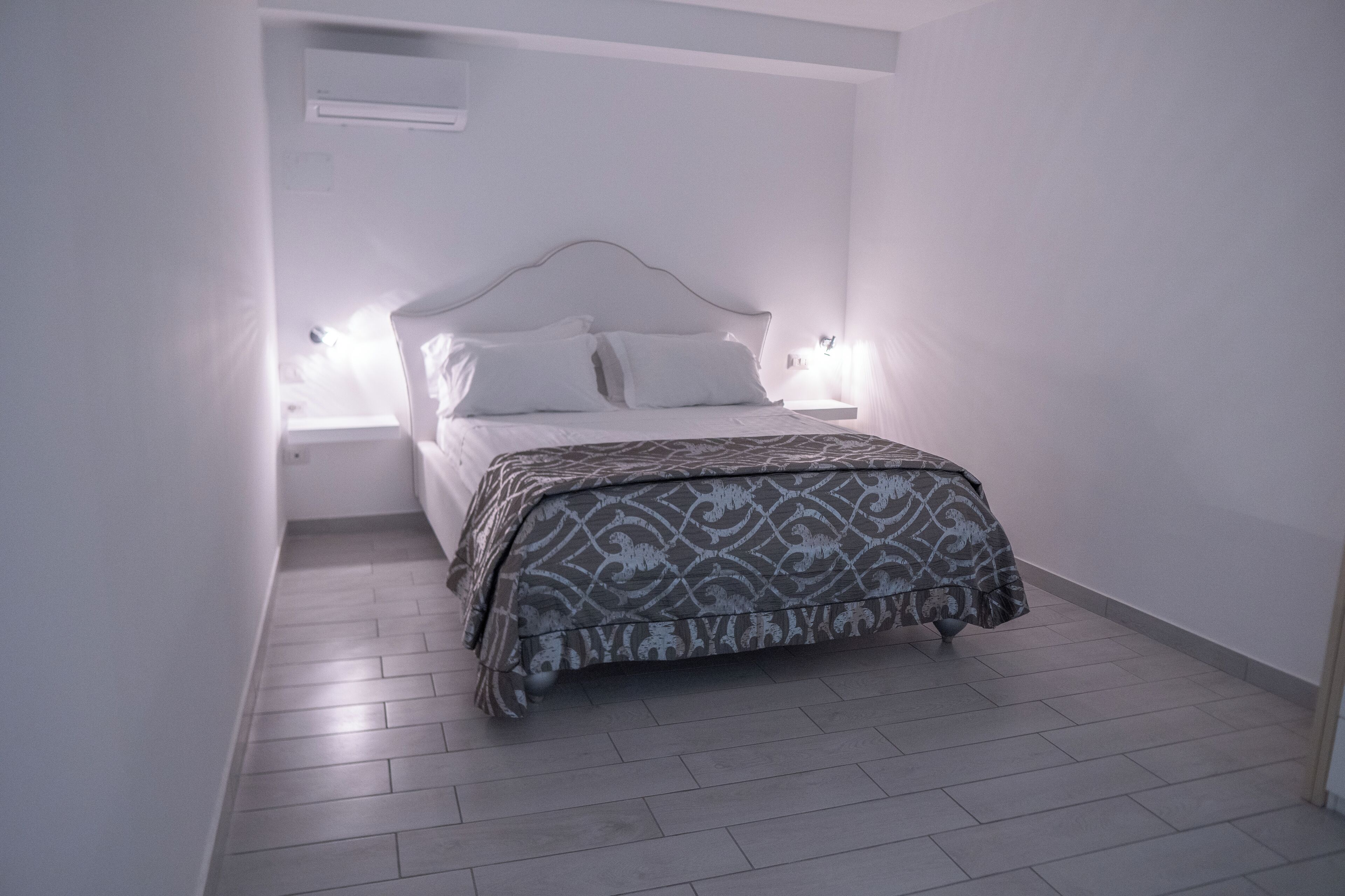 A bedroom with a bed, bedside tables, and a wall-mounted air conditioner.