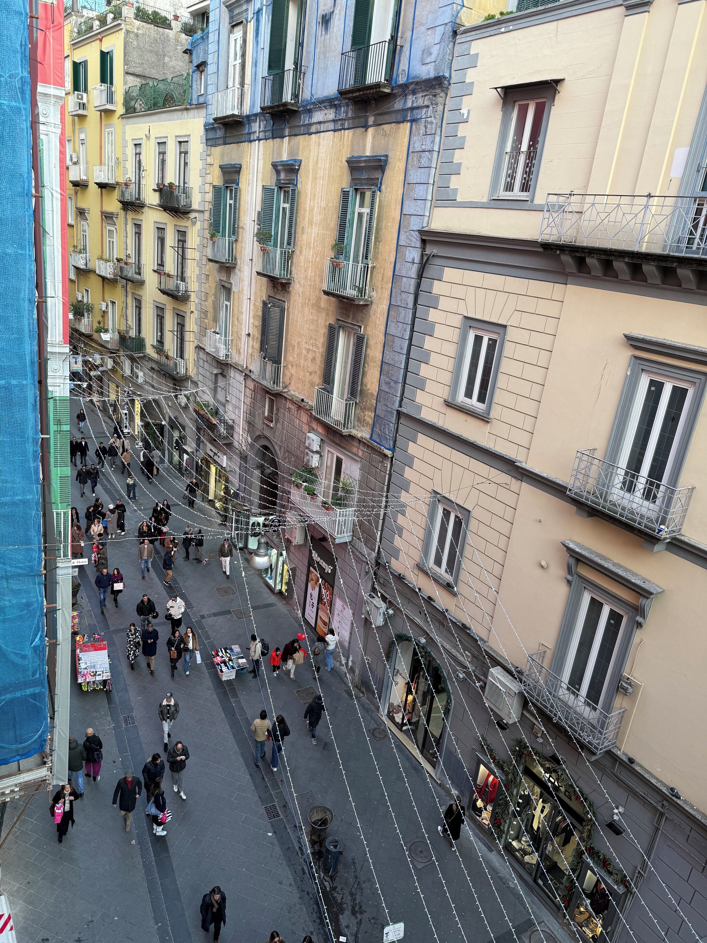 A street view with multiple buildings, balconies, and pedestrians.