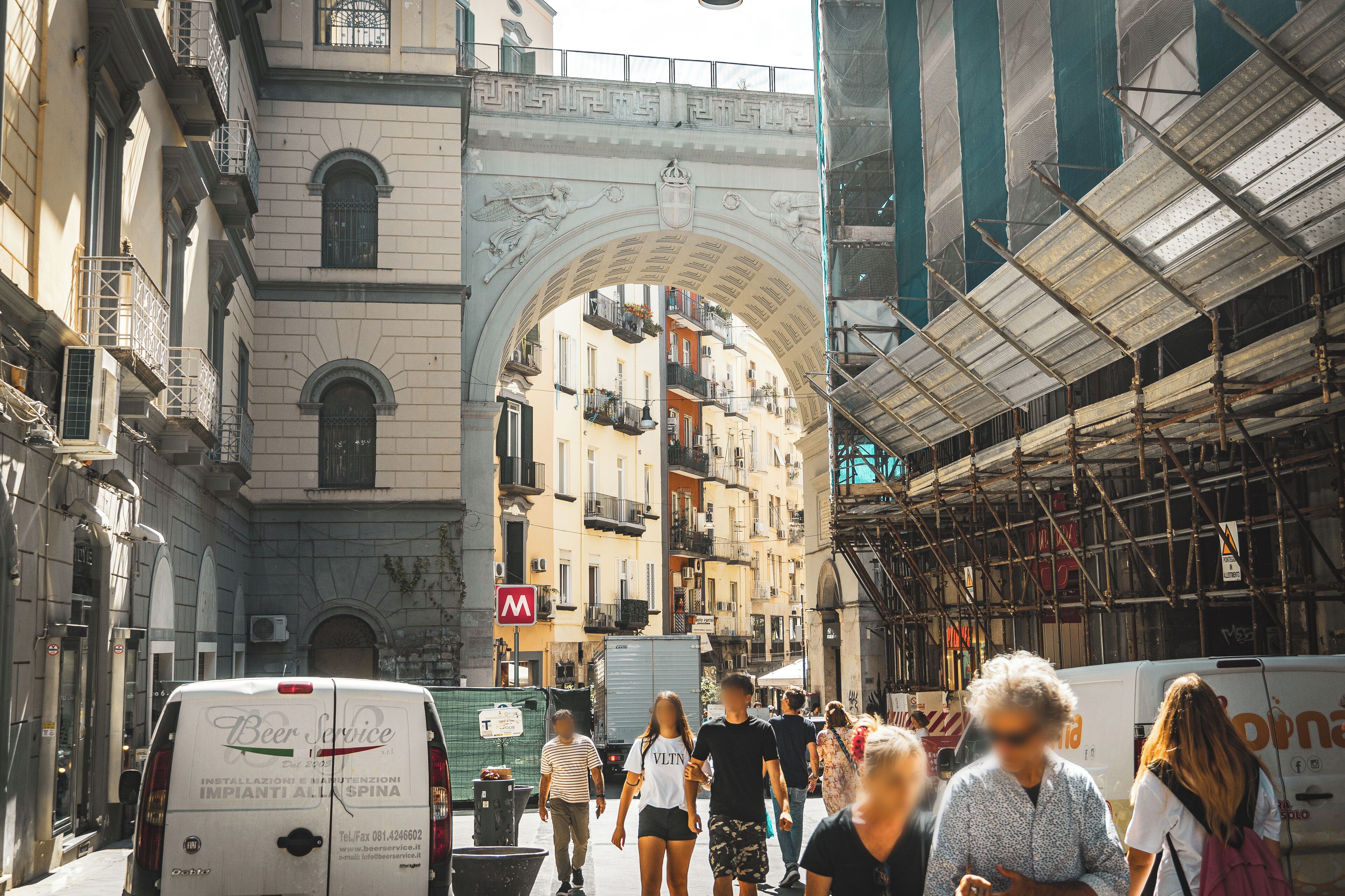 A busy urban street with an ornate archway, a white van, and pedestrians.