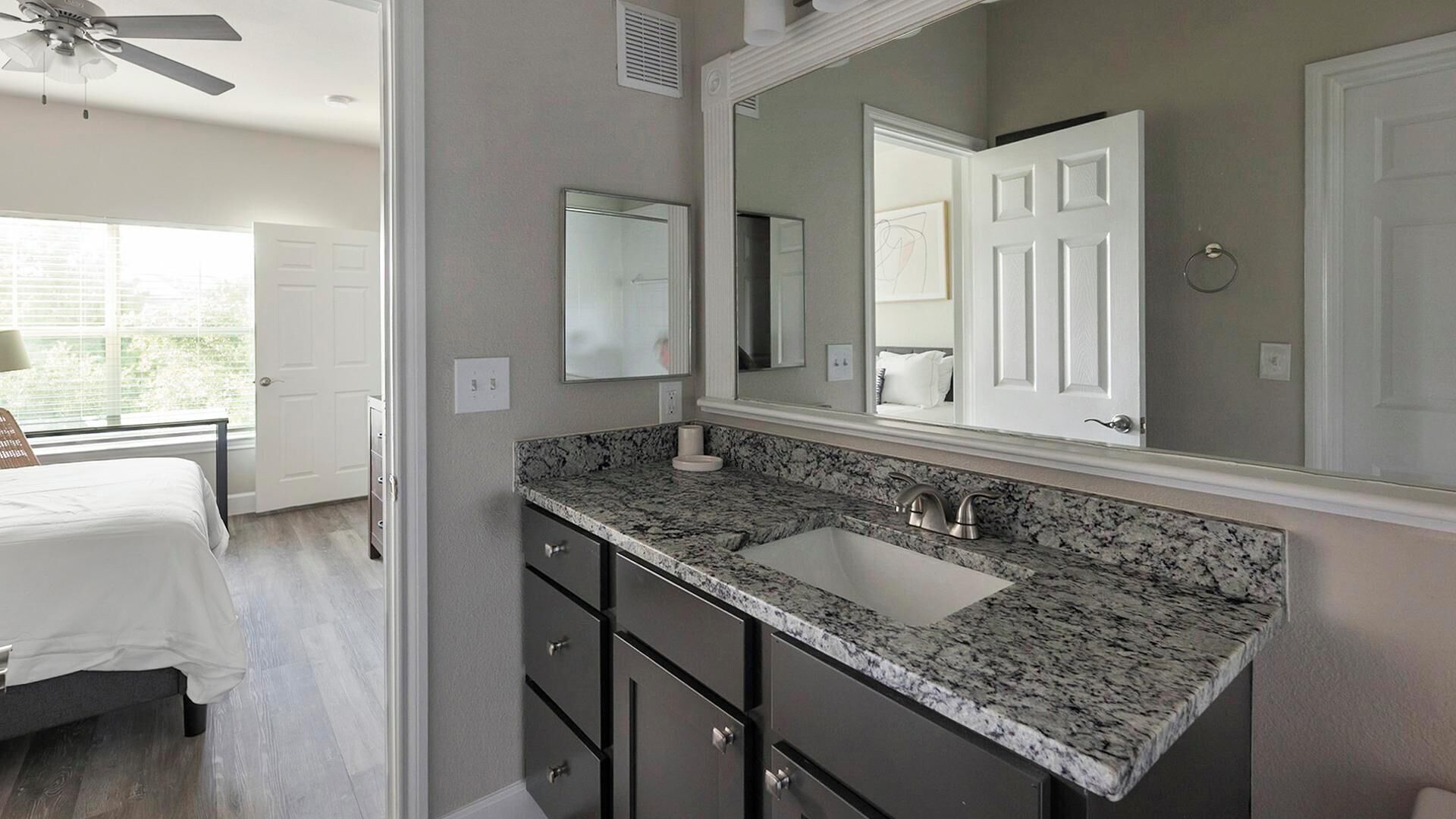 A modern bathroom with a large mirror, dark cabinetry, and a granite countertop.