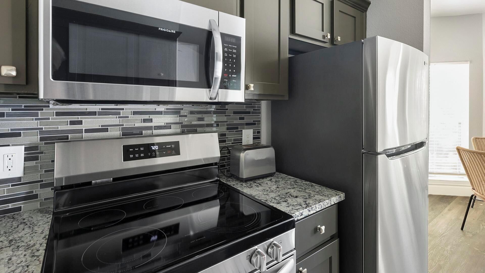A modern kitchen with a stainless steel refrigerator, a microwave, an oven, and a toaster.