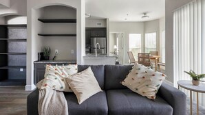 A modern living room with a grey sofa, decorative pillows, and a small round table with a plant.