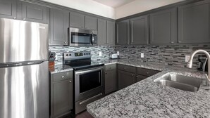 Una cocina moderna con electrodomésticos de acero inoxidable, encimera de granito y salpicadero de azulejos.