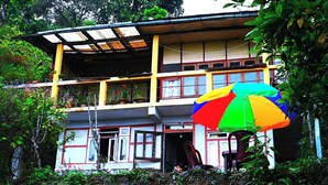Un edificio de dos pisos con un balcón, un paraguas colorido y una puerta abierta hacia un lado.