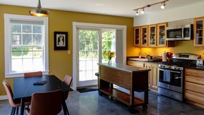 Una cocina con comedor, armarios de madera, microondas, estufa y un amplio ventanal con vistas a zonas verdes.