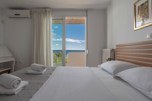 A hotel room with a bed, a desk, a chair, a window with curtains, and a view of the sea. - NG Villas Polichrono (Kassandra)
