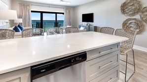 Una cocina moderna con una isla central, lavavajillas y un comedor con sillas de mimbre.