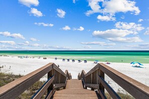 A wooden staircase leading to a beach with umbrellas and beachgoers.
