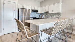 Una cocina moderna con armarios blancos, un refrigerador de acero inoxidable, un microondas y una isla grande con taburetes de bar.