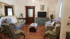Een woonkamer met een bank, twee fauteuils, een salontafel, een televisie en een kast.