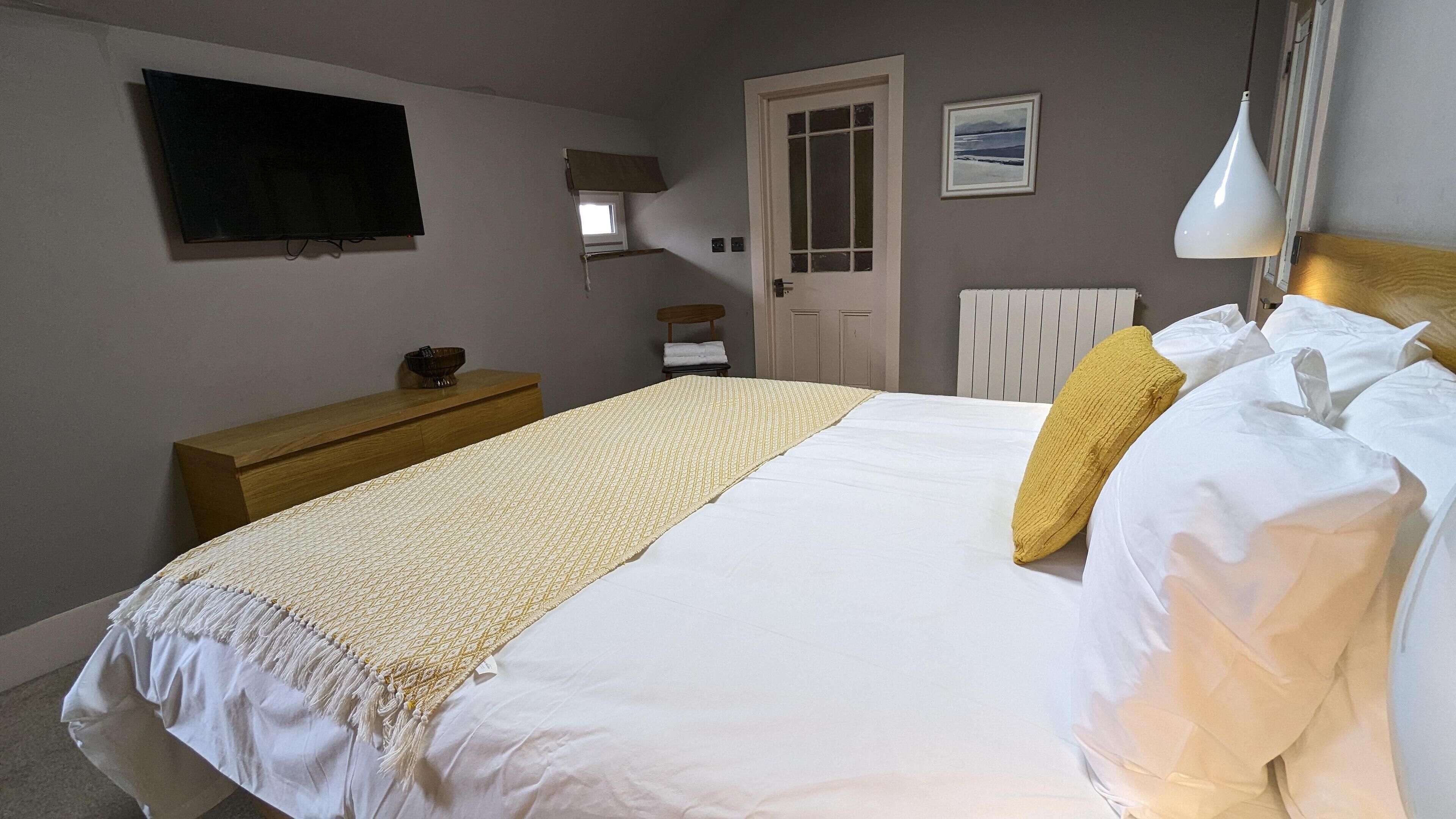 Une chambre à coucher avec un lit, une commode en bois, un téléviseur, une porte et un radiateur.