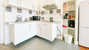 Moderni keittiö, jossa on valkoiset kaapit, ruostumattomasta teräksestä valmistettu pesuallas, mikroaaltouuni ja kahvinkeitin.